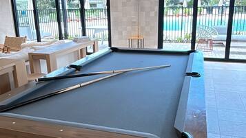 A pool table in a room with large windows, a bench, and a view of a pool outside.