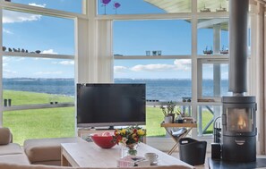 Ein Zimmer mit großem Fenster mit Blick auf ein Gewässer, einem Fernseher, einem Kamin und einem Tisch mit einer Blumenschale.