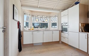 Eine moderne Küche mit weißen Schränken, einem eingebauten Ofen und einem Fenster mit Vorhängen.