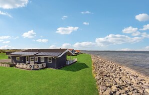 Ein Küstenanwesen mit einer Rasenfläche, einer Holzterrasse und Blick auf das Meer.