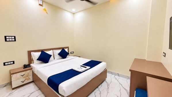 A hotel room with a bed, bedside table, and a small desk.