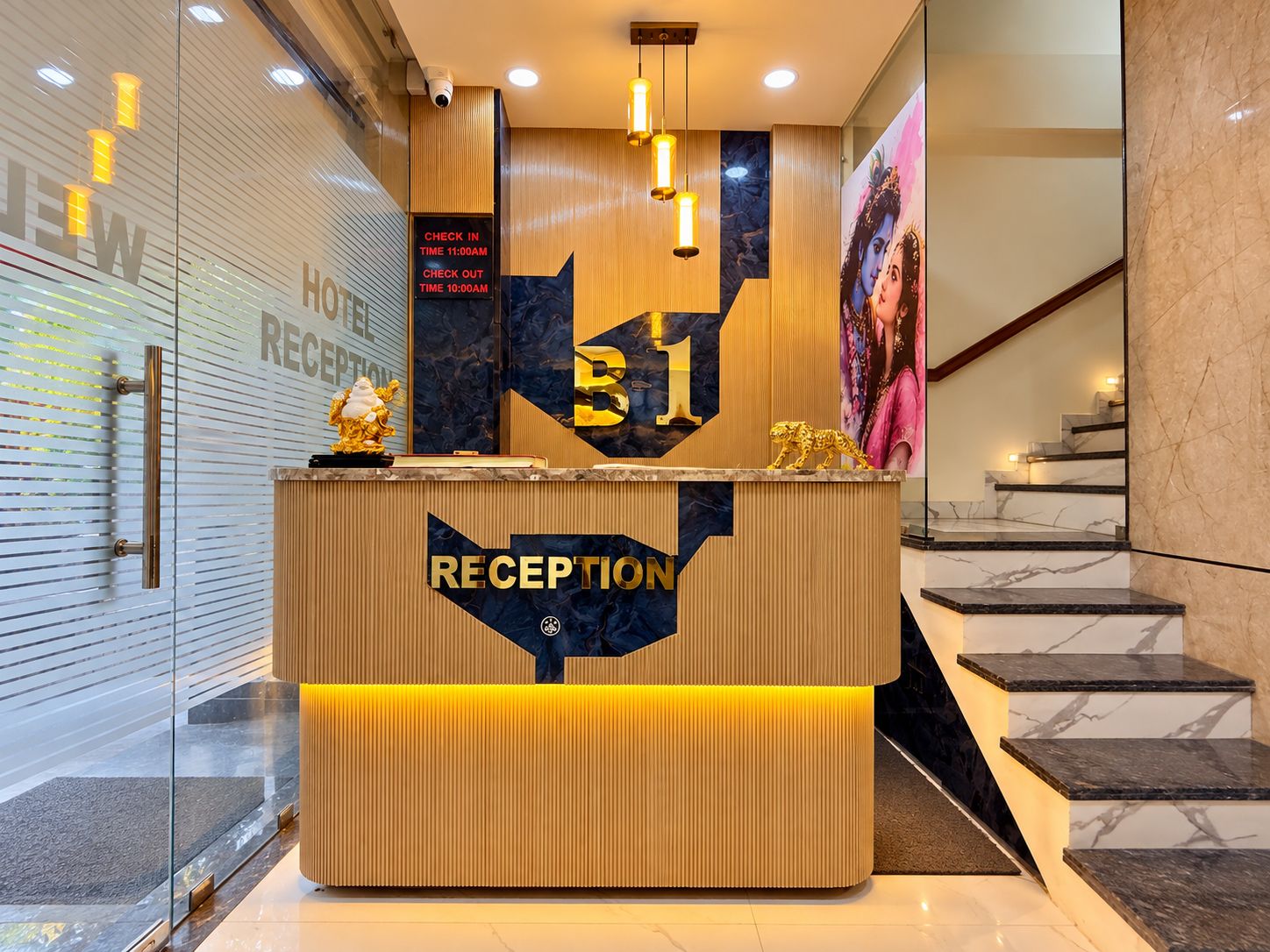 A hotel reception desk with a check-in/out time display, a reception area, and a staircase.