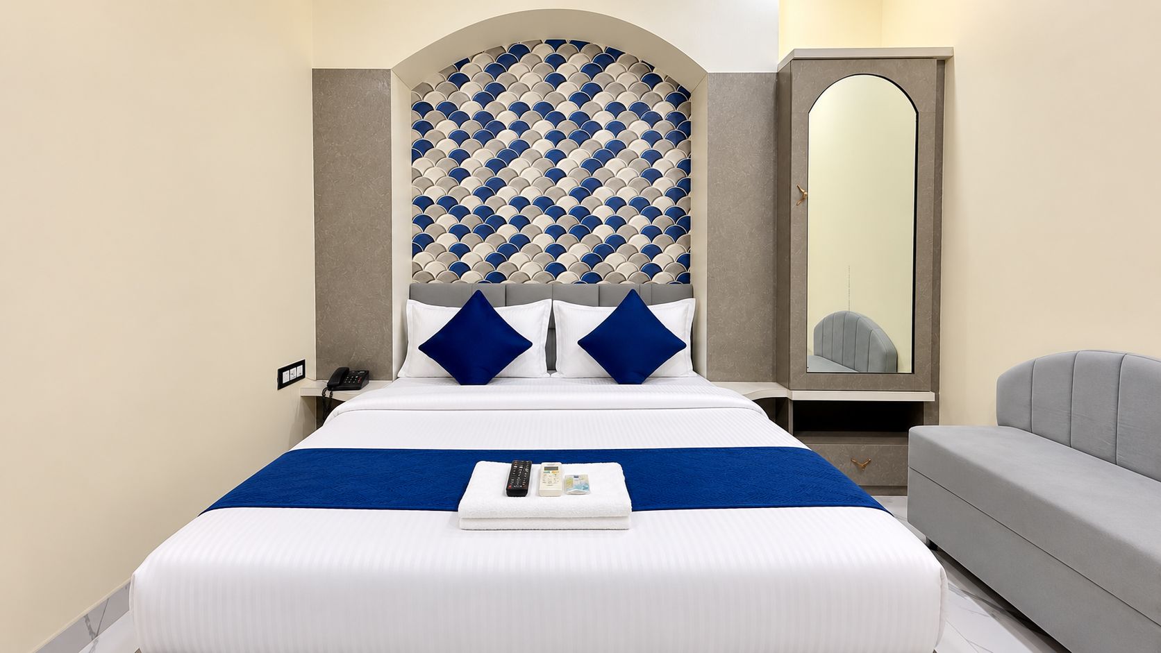 Habitación de hotel con una cama grande, una mesita de noche, un espejo y un espacio para sentarse.