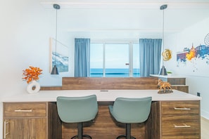 A modern kitchen with a view of the sea, featuring two bar stools, a vase with orange flowers, and a decorative horse statue. - Endless Ocean Views at Yachtsman S904 (Myrtle Beach)
