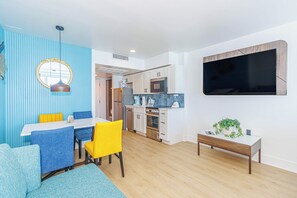 Ett kompakt bostadsutrymme med en matplats, ett litet kök och en platt-TV som är monterad på väggen.