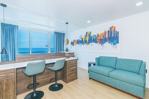 A modern living room with a sofa, a dining area with a bar, and a cityscape painting on the wall. - Endless Ocean Views at Yachtsman S904 (Myrtle Beach)