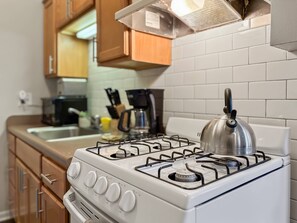 A kitchen with a white gas stove, wooden cabinets, a coffee maker, and a kettle.