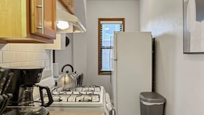 Une cuisine compacte équipée d’une cuisinière à gaz, d’une bouilloire et d’une poubelle.