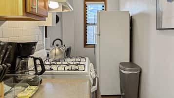 A compact kitchen with a gas stove, kettle, and a trash bin.