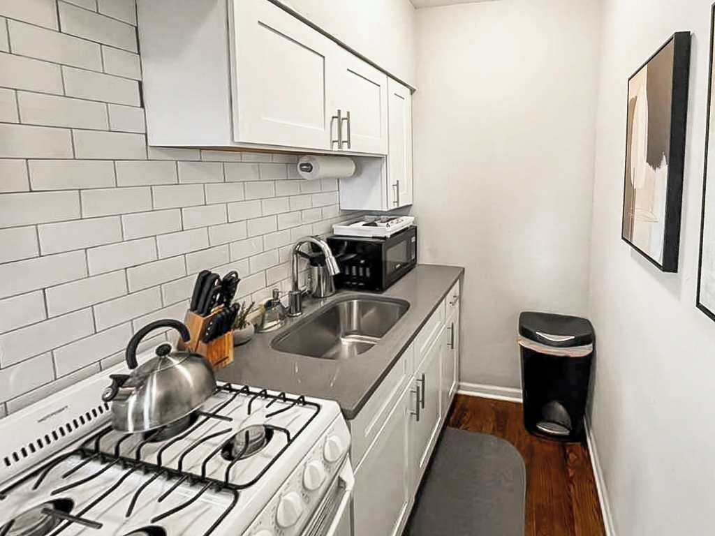 A compact kitchen with white cabinets, a gas stove, a sink, and a trash bin.
