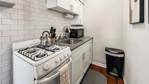 A compact kitchen with white cabinets, a gas stove, a microwave, and a trash bin. - Cozy Well-Equipped Studio Apartment (Chicago)