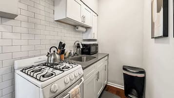 Uma cozinha compacta com armários brancos, fogão a gás, micro-ondas e lixeira.