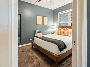 Un dormitorio con cama, mesita de noche, lámpara y ventana con persianas.