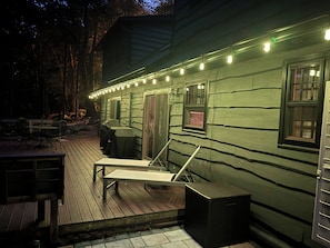 A wooden deck with a covered seating area and a grill, surrounded by a house with a green exterior and string lights. - Rustic Elegance Wrapped in Nature!   

3-bedroom Cabin in Serene Lake Harmony (Lake Harmony)