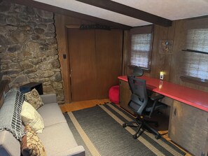 A room with a stone wall, a wooden door, a red desk, a black office chair, a grey sofa with patterned cushions, and a striped rug. - Rustic Elegance Wrapped in Nature!   

3-bedroom Cabin in Serene Lake Harmony (Lake Harmony)
