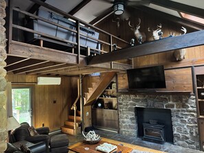 A spacious living area with a stone fireplace, a television mounted above it, and a wooden staircase leading to an upper level. - Rustic Elegance Wrapped in Nature!   

3-bedroom Cabin in Serene Lake Harmony (Lake Harmony)