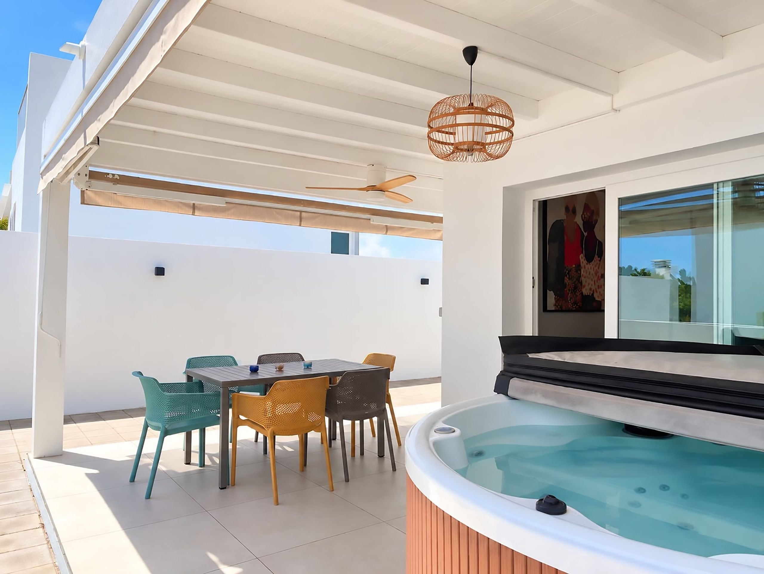 Un patio exterior moderno con un jacuzzi, una mesa de comedor con sillas y un ventilador de techo.