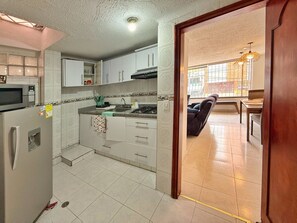 Una cocina con armarios blancos, microondas y estufa a gas. Hay una zona de comedor con una silla y una mesa.