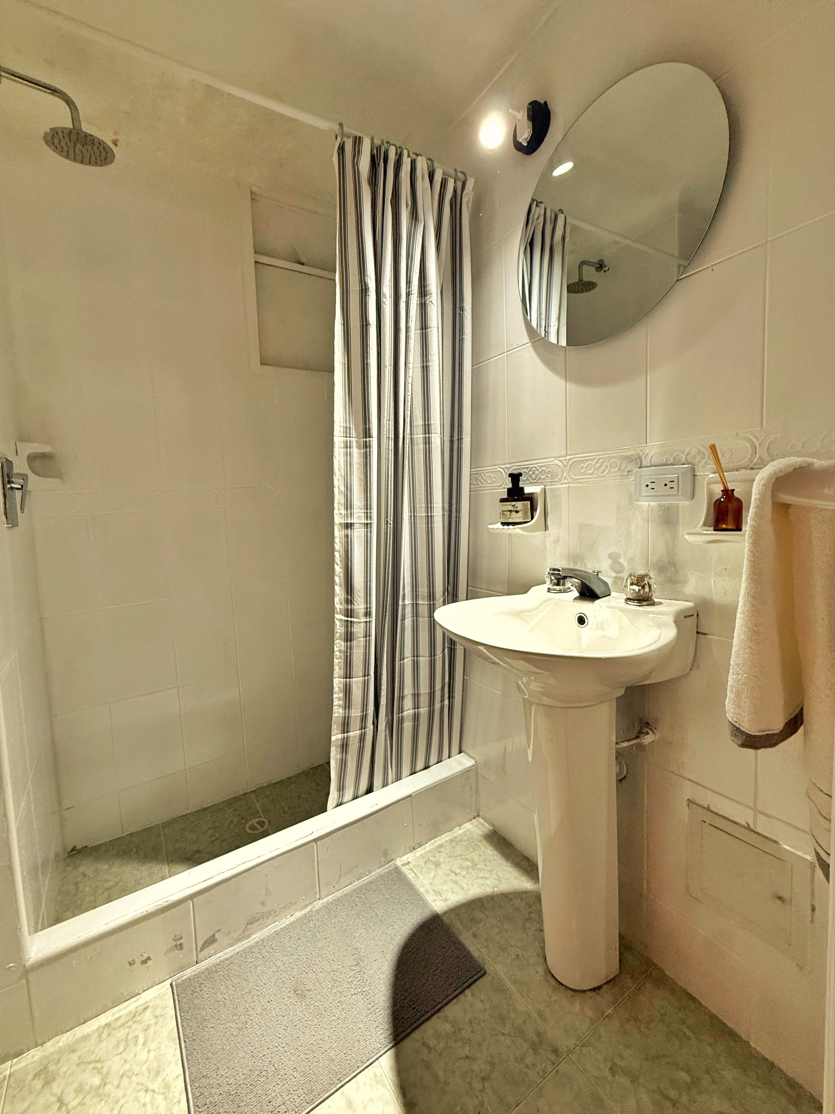 A bathroom with a shower, a sink, a mirror, and a towel rack.