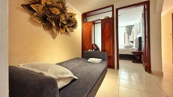 A room with a bed, a sofa, a decorative wall piece, and a door leading to another room.