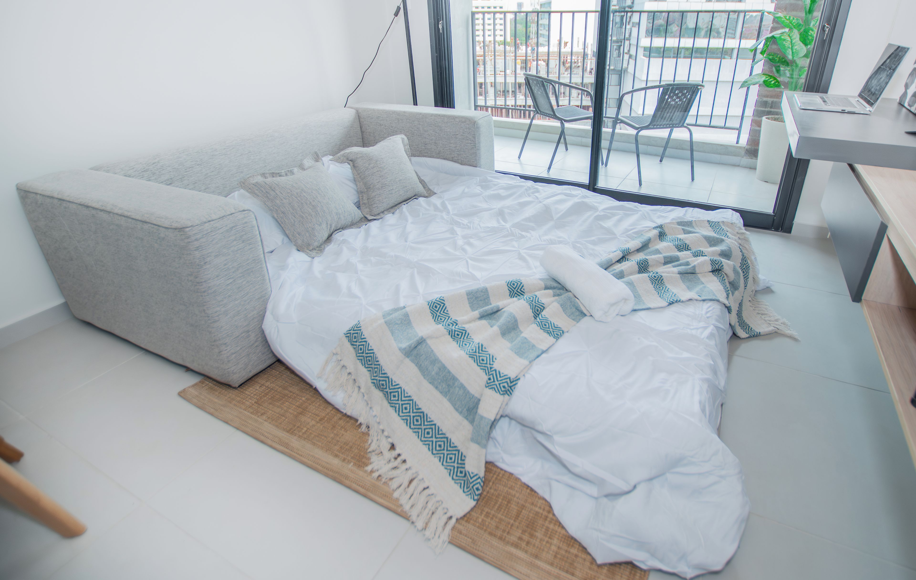 A modern bedroom with a grey sofa bed, a white bedspread, and a patterned throw.