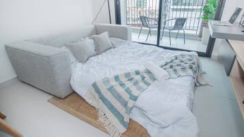 A modern bedroom with a grey sofa bed, a white bedspread, and a patterned throw.
