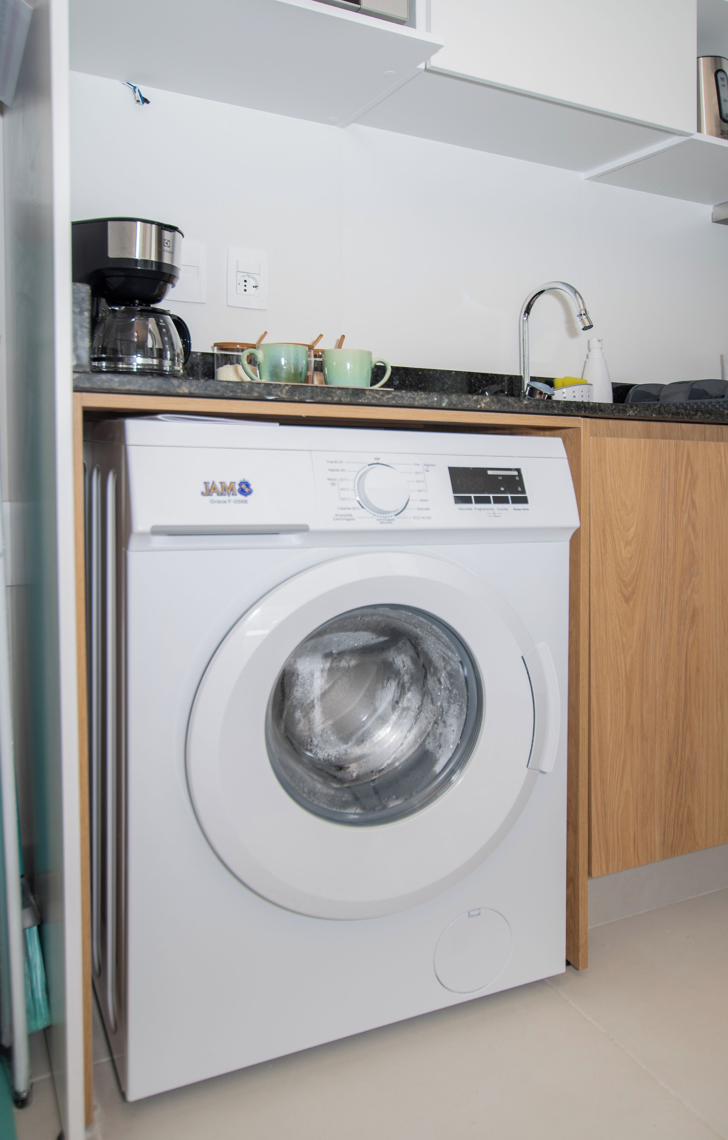 A front-loading washing machine in a kitchen with a countertop, a coffee maker, and a sink.