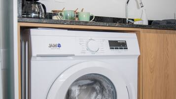 A front-loading washing machine in a kitchen with a countertop, a coffee maker, and a sink.