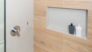 A modern bathroom with a shower, a wooden wall, and a shelf with toiletries. - Corporate Stays First del Sol - 707 (Asunción)