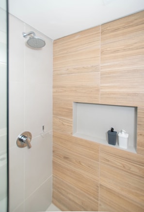 A modern bathroom with a shower, a wooden wall, and a shelf with toiletries. - Corporate Stays First del Sol - 707 (Asunción)