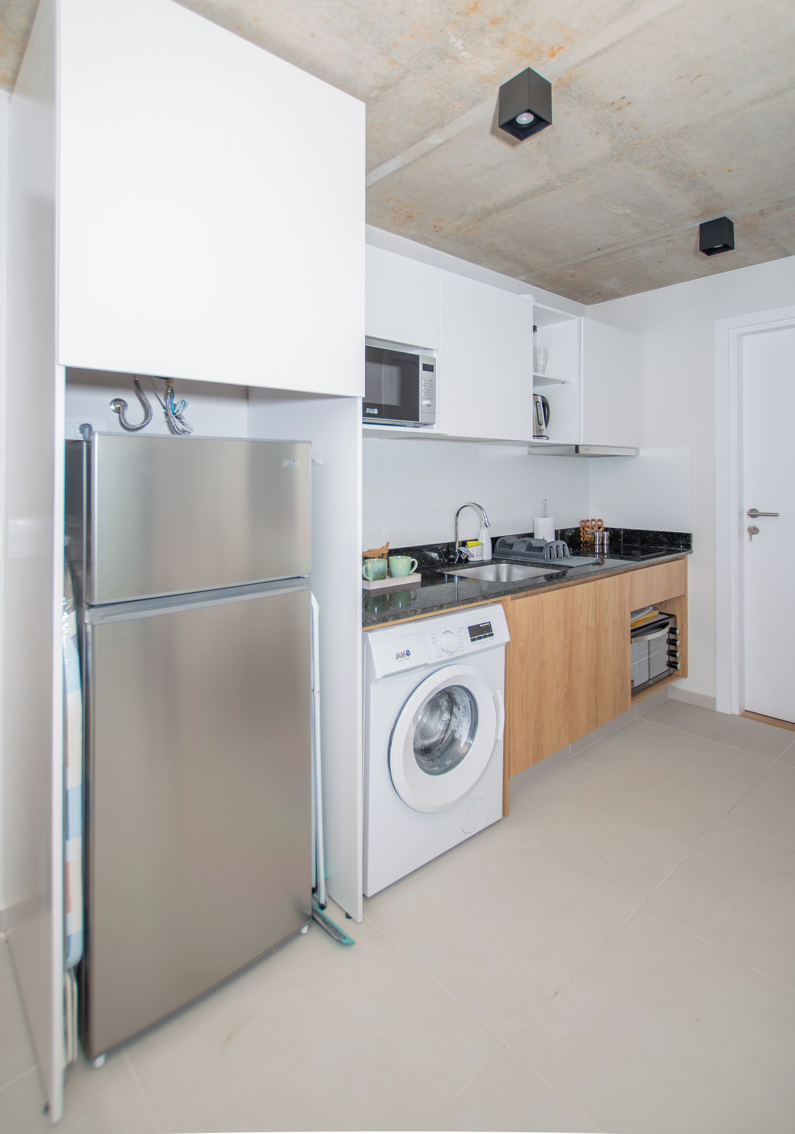 A modern kitchen with a stainless steel refrigerator, a washing machine, and a microwave.