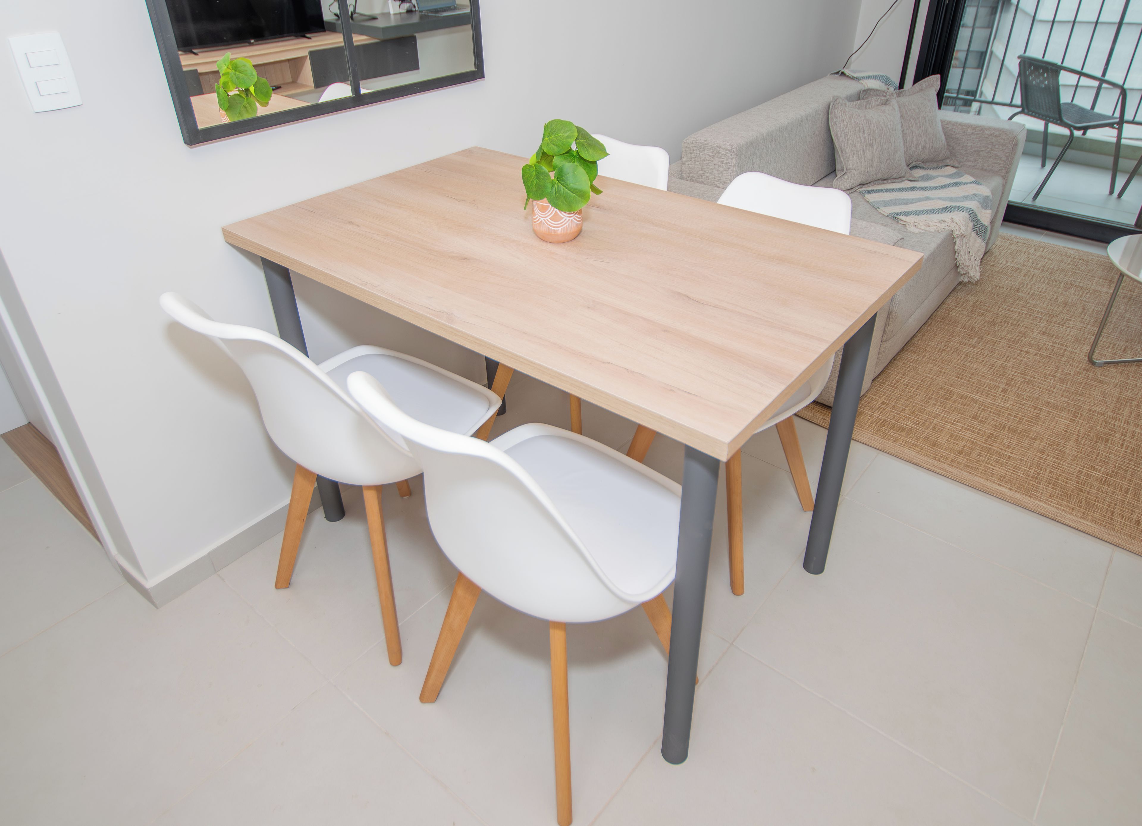 Un comedor con una mesa de madera, dos sillas blancas y una planta en maceta.