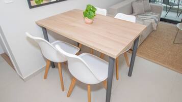Un comedor con una mesa de madera, dos sillas blancas y una planta en maceta.