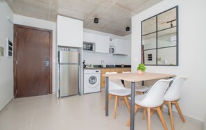 Cocina compacta con lavadora, refrigerador y comedor con sillas y mesa.