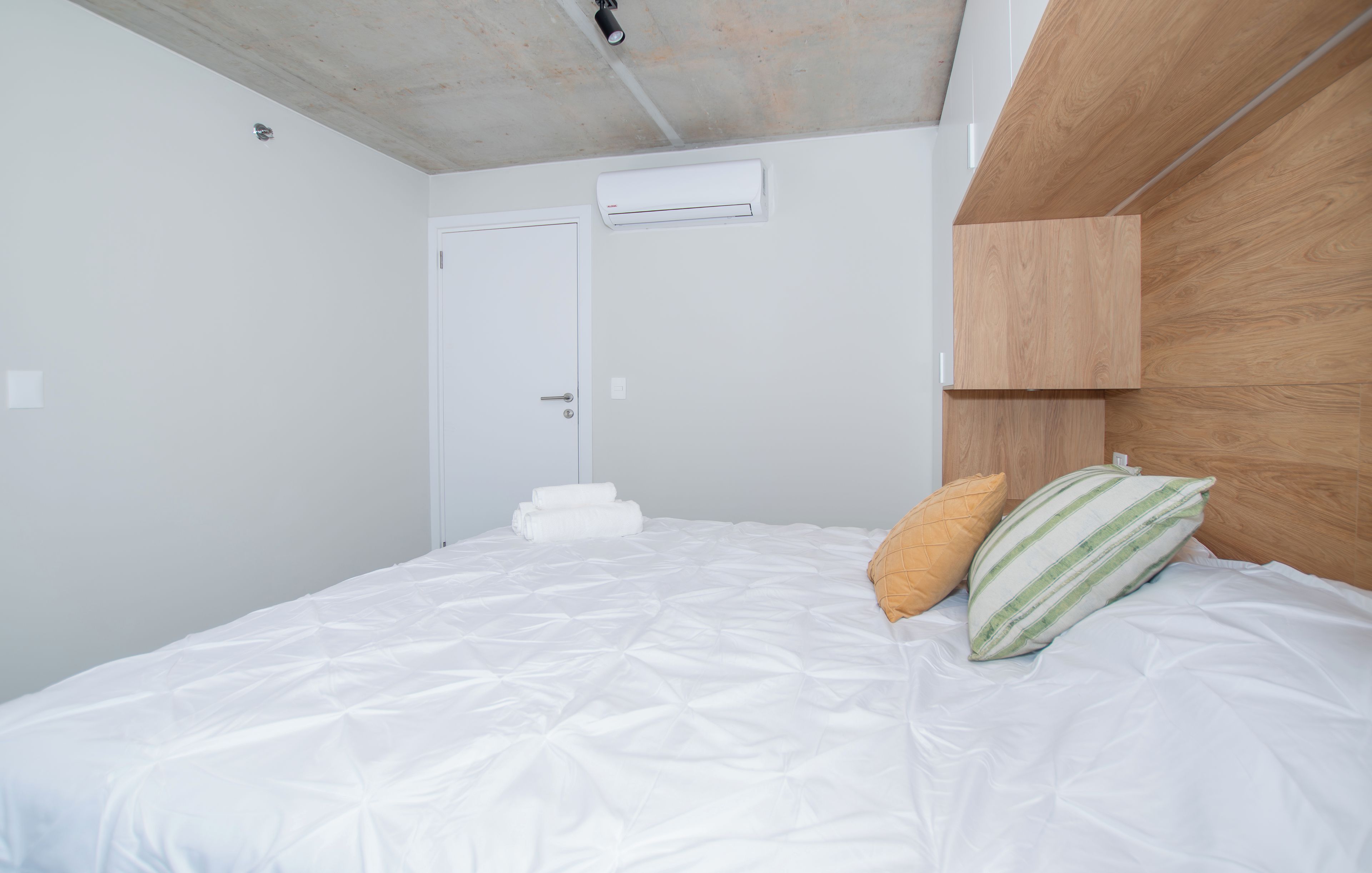 Un dormitorio con una cama, almohadas, un cabecero de madera y una puerta blanca.