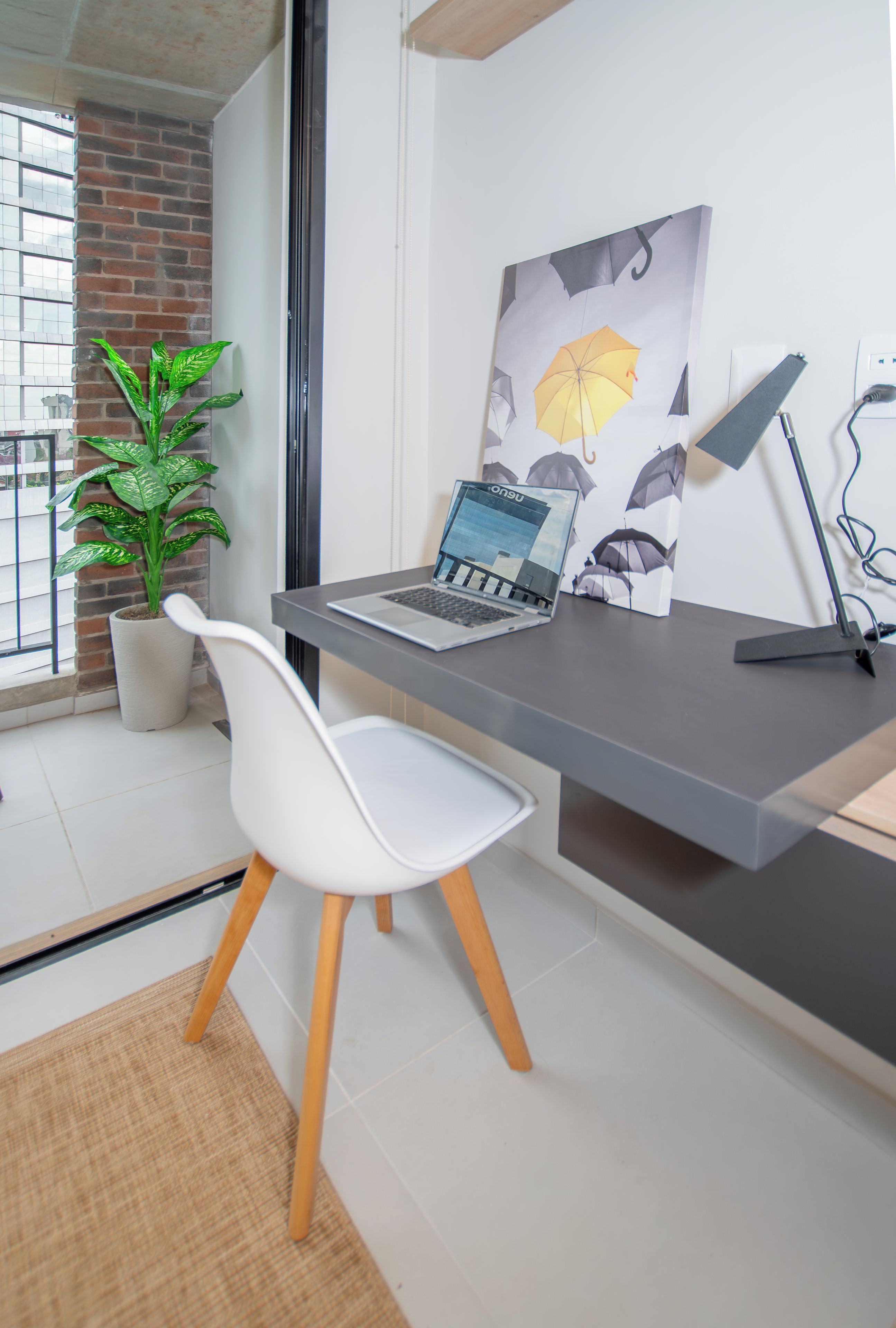 Een moderne kantoorruimte met een bureau, een laptop, een witte stoel, een potplant en een schilderij van parasols.