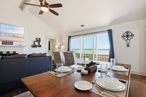 Ein Essbereich mit einem Holztisch, gedeckt für vier Personen, einer Couch und Blick auf den Strand.