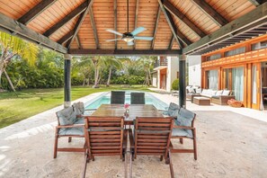 An outdoor seating area with a pool, wooden furniture, and a covered patio. - Amazing villa w/ pool/maid/BBQ at Green Village (Punta Cana)