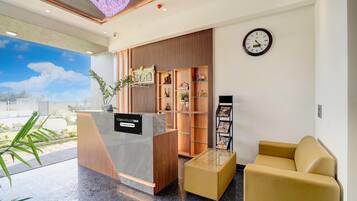 A reception area with a reception desk, a clock, a sofa, and a wall with shelves.