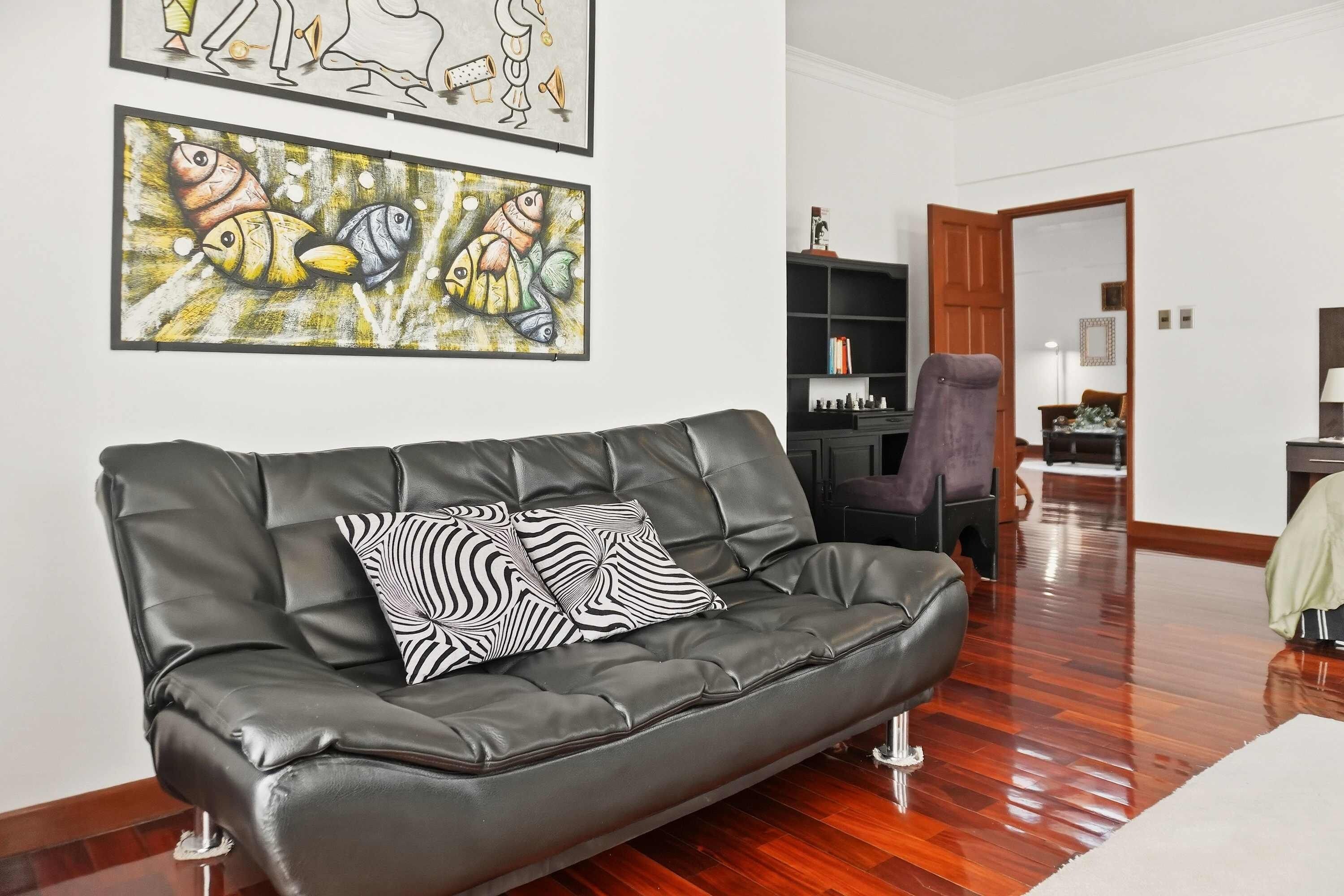 A living room with a black leather sofa, two zebra-patterned cushions, and two abstract fish paintings on the wall.