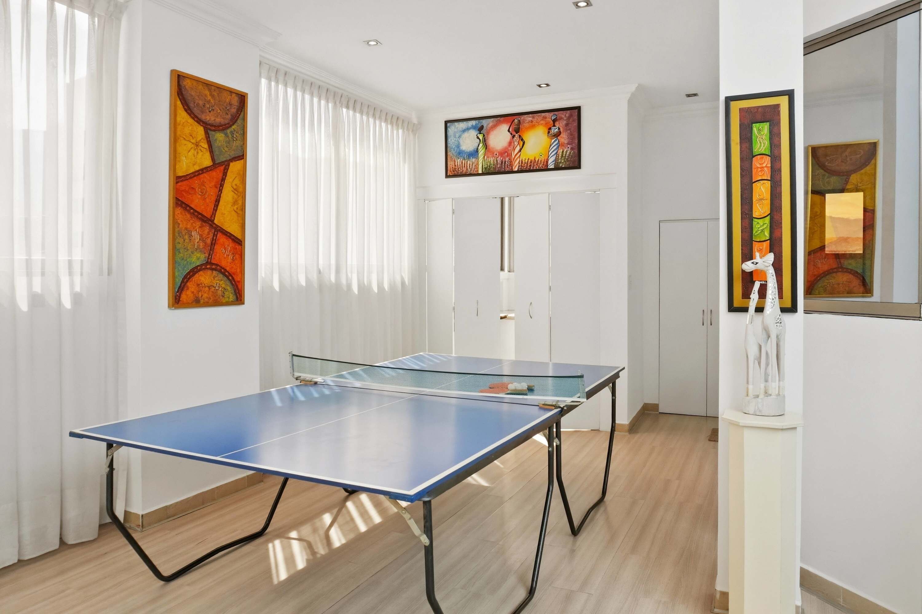 Una habitación con dos mesas de ping pong, paredes blancas y obras de arte.