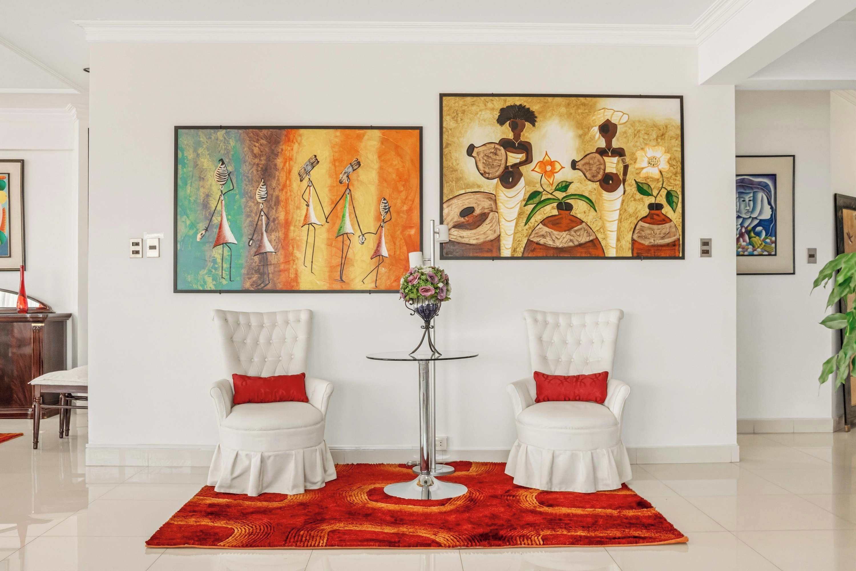 A room with two white armchairs, a red rug, and two paintings on the wall.