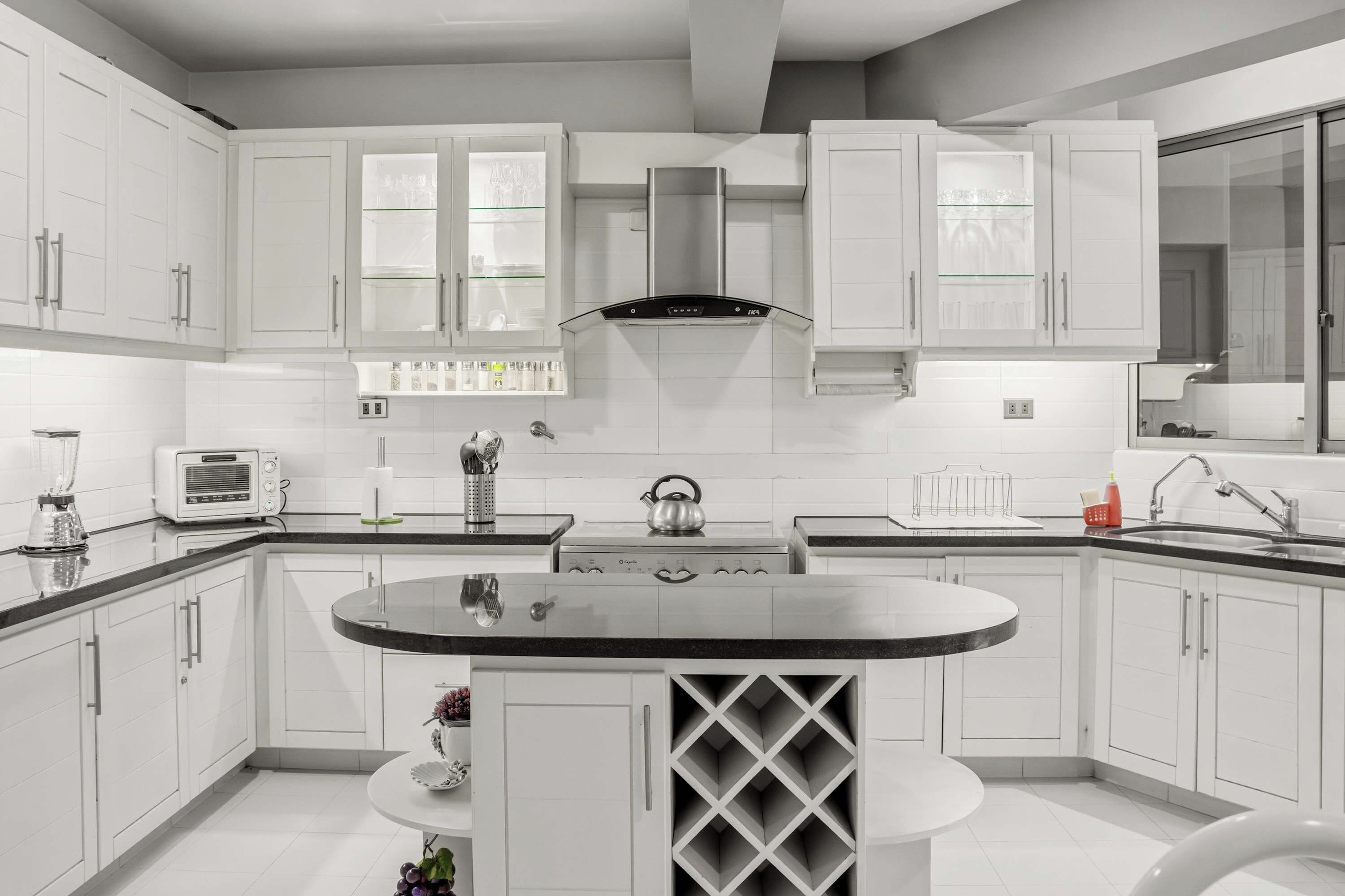 Una cocina moderna con armarios blancos, una isla central y una vinoteca empotrada.