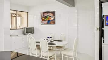 A modern kitchen with white cabinetry, a dining table with chairs, a flat-screen TV, and a painting on the wall.