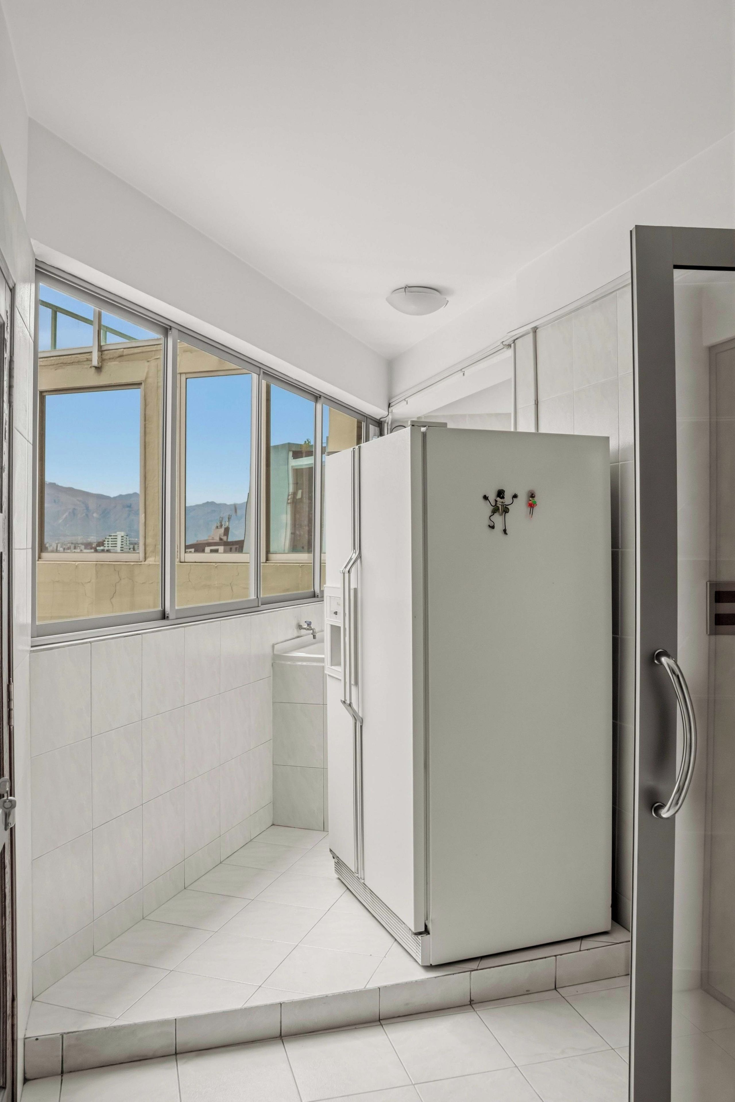 A modern bathroom with a large window, a white bathtub, and a white refrigerator.