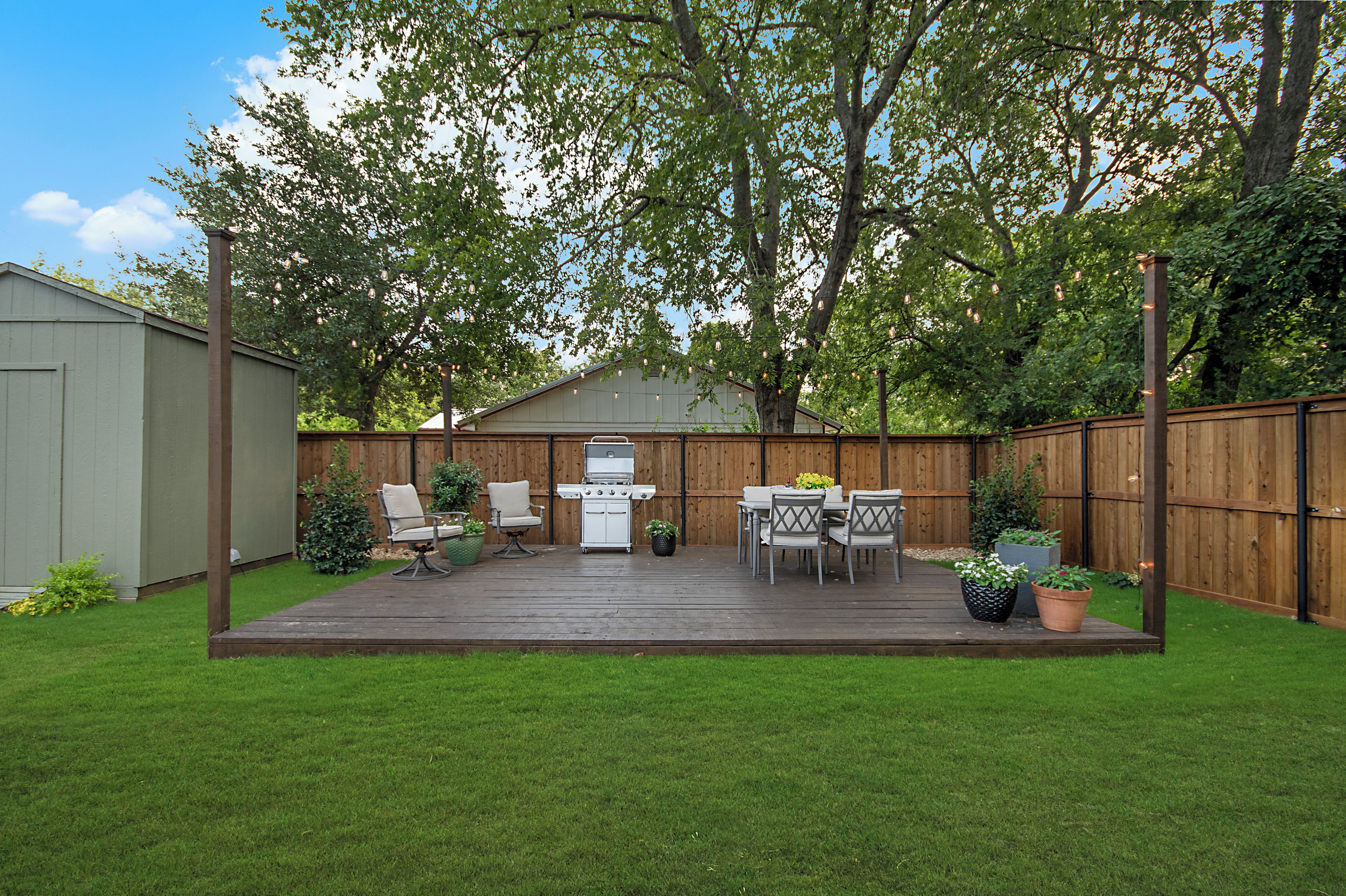 Ein Garten mit einer Holzterrasse, einem Grill, Gartenmöbeln und einem Holzzaun.