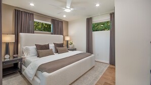 Quarto moderno com cama grande, duas mesas de cabeceira, ventoinha no teto e vista para o verde pela janela.