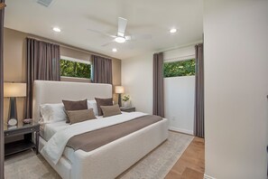 A modern bedroom with a large bed, two bedside tables, a ceiling fan, and a view of greenery through the window. - Close to UNT & TWU.  Easy stays for college families! (Denton)