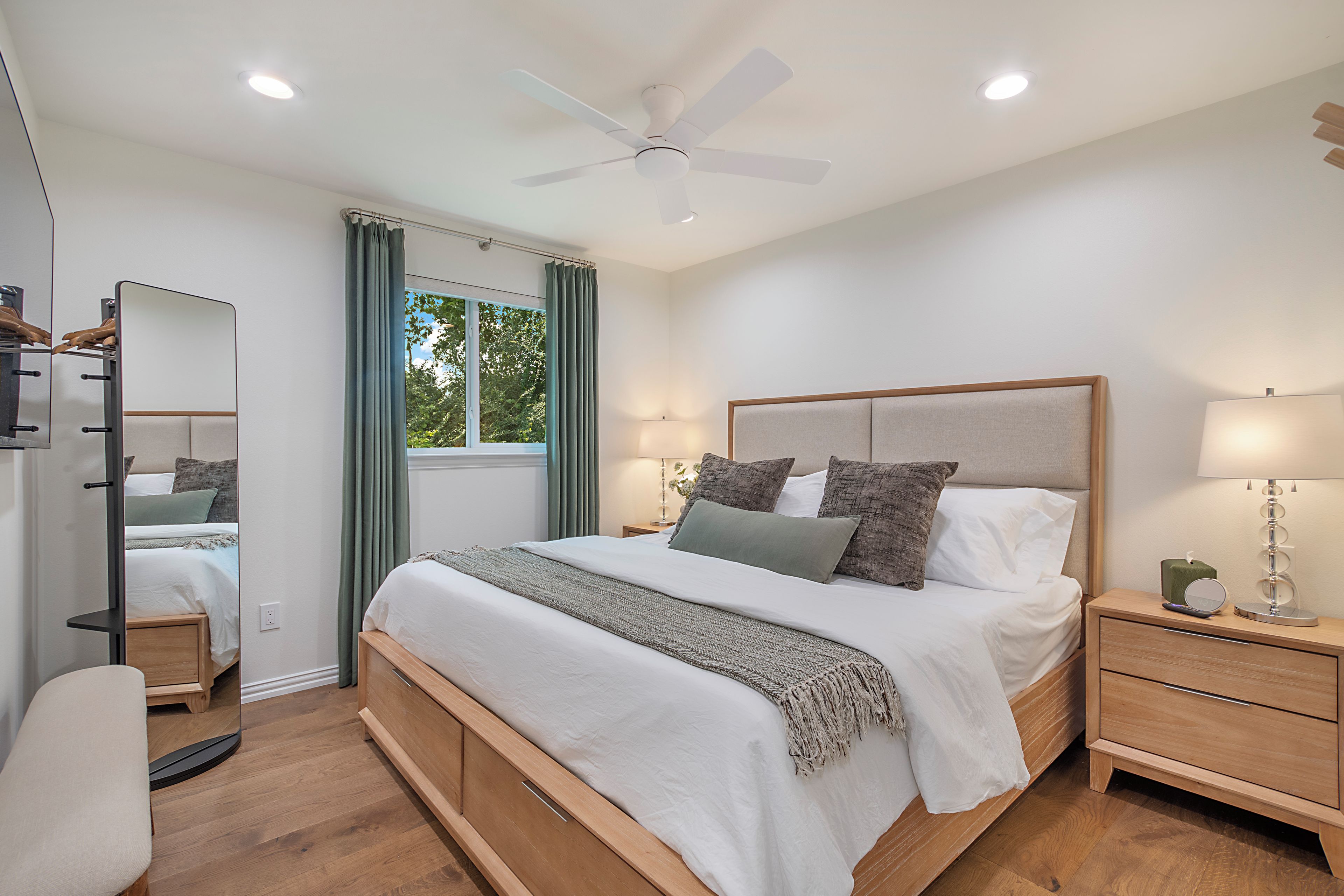 A modern bedroom with a large bed, bedside lamps, a ceiling fan, and a window with curtains.