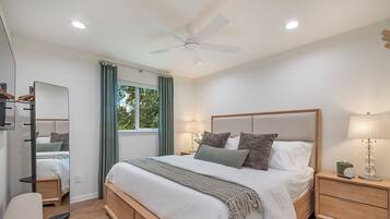 A modern bedroom with a large bed, bedside lamps, a ceiling fan, and a window with curtains.